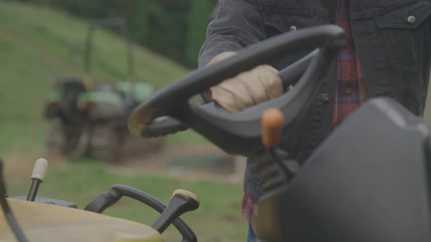 The man walks over and gets on the riding mower