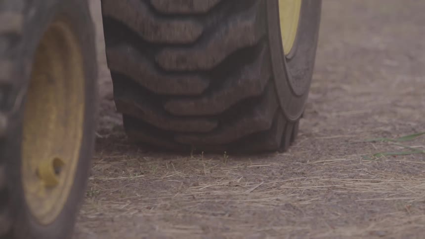 The video shows the large heavily treaded tires of a john deere tractor the tractor is either driving slowly or stationary on what looks like a dry dusty field