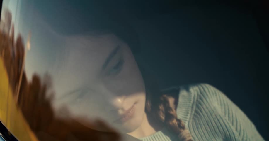 Woman with a braid reflected in the car window looking down with a calm expression