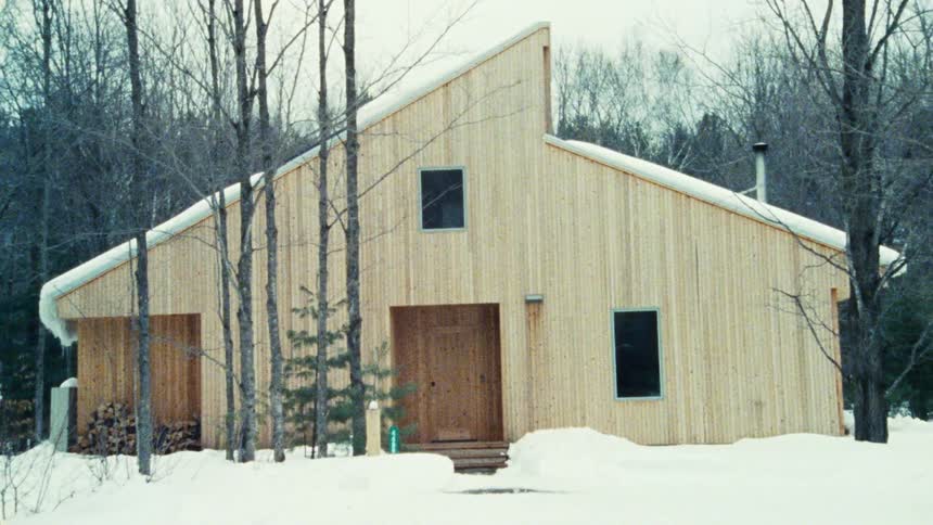 Light wooden cabin surrounded by snow and leafless trees