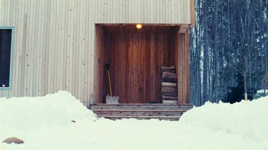 Wooden cabin entrance with a stack of firewood and a snow shovel surrounded by piledup snow