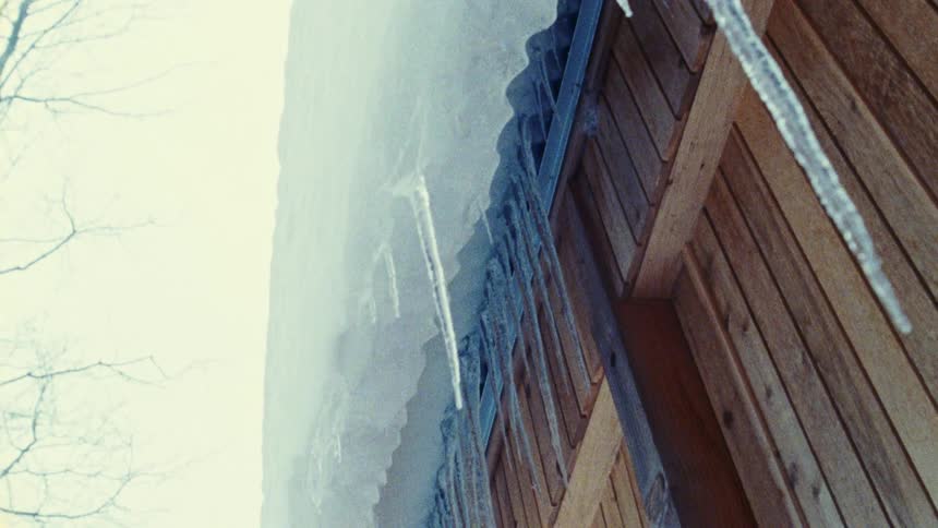A wooden cabin roof with icicles hangs over a snowy winter