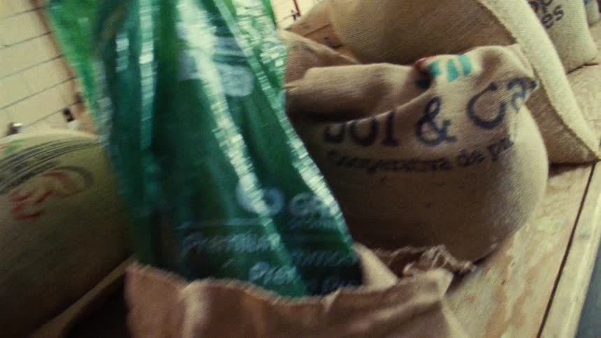 A camera moves through a warehouse showing large burlap bags of coffee beans stacked on wooden pallets