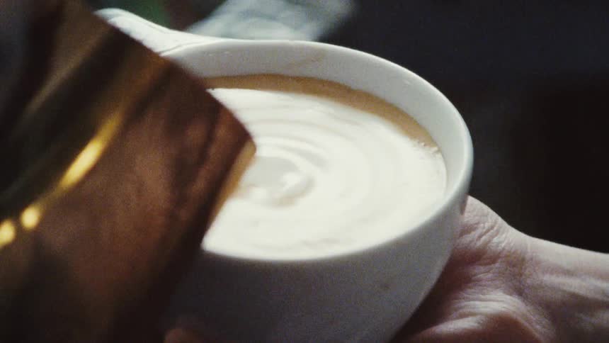 A barista carefully pours cream into an espresso beverage
