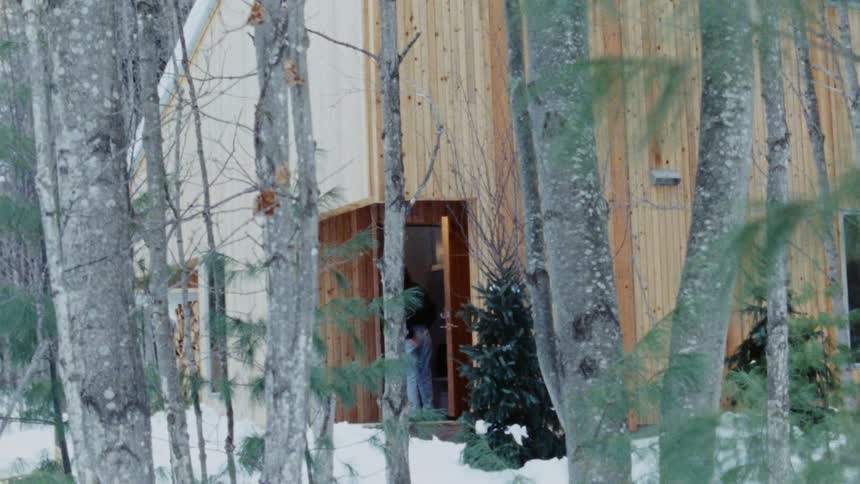 A couple walks into their home through the back door on a winter day surrounded by trees