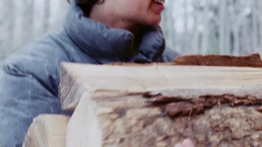 A woman picking up firewood and placing it in a mans hands