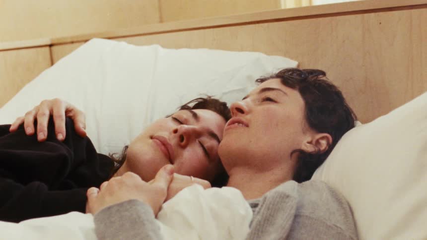A lesbian couple cuddles together in bed