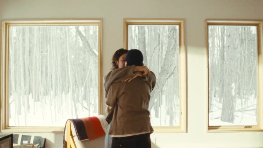Couple embraces in a bright room with windows facing the snow