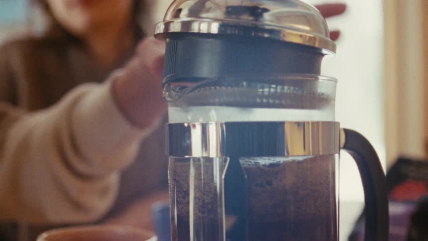 Hand pressing the plunger of a french press with freshly brewed coffee