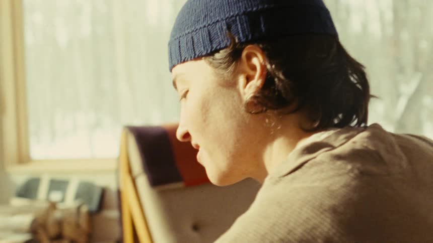 A man playing a guitar for a woman who is sitting holding a book and smiling