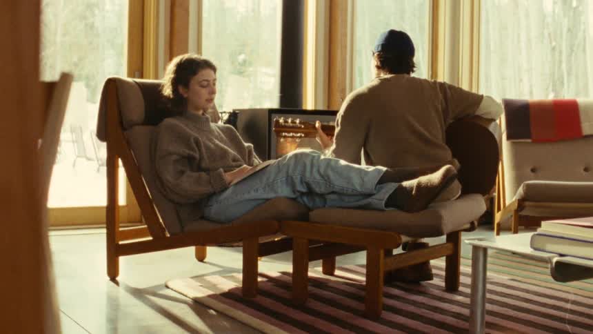 The woman is playing guitar in front of the fireplace