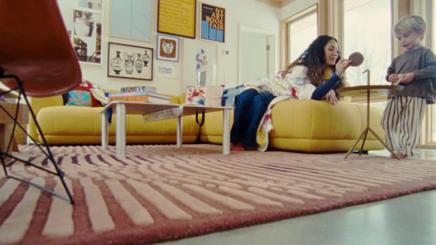 Woman lying on a yellow sofa interacting with a child in a room decorated with paintings