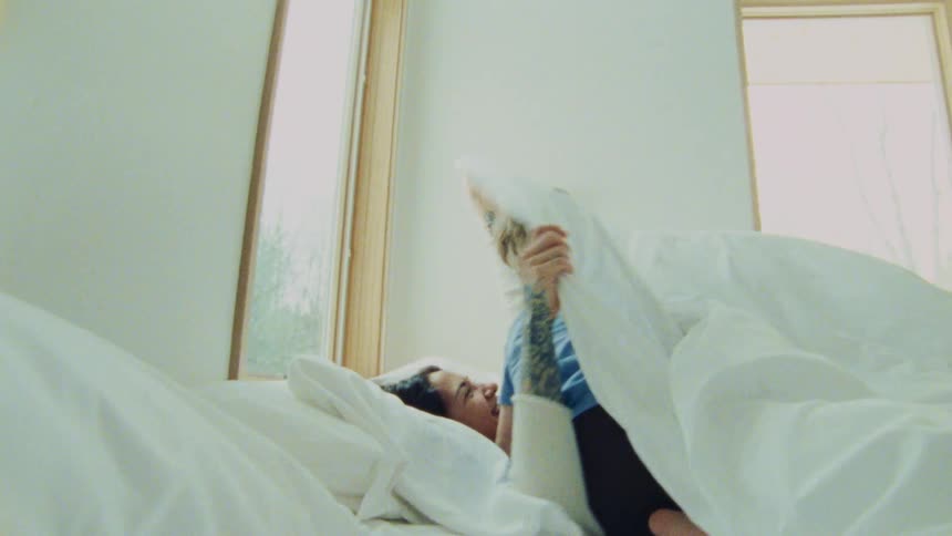 A playful and joyful moment between an adult and a child in bed as the child playfully interacts and hides under the covers