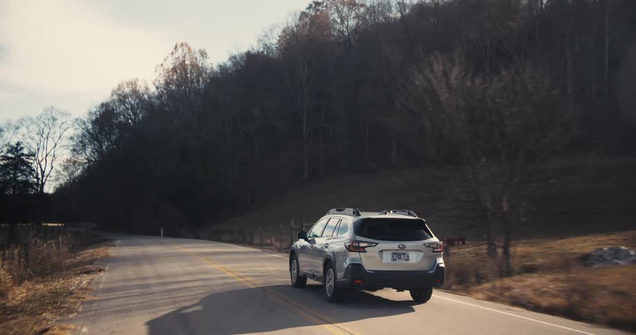 A car is driving down a rural highway through a forest