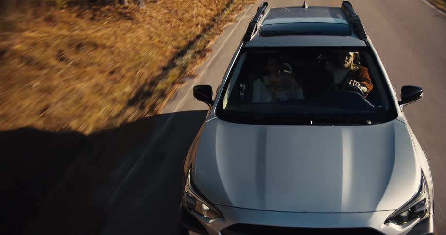 A person is driving a silver subaru car along a rural street