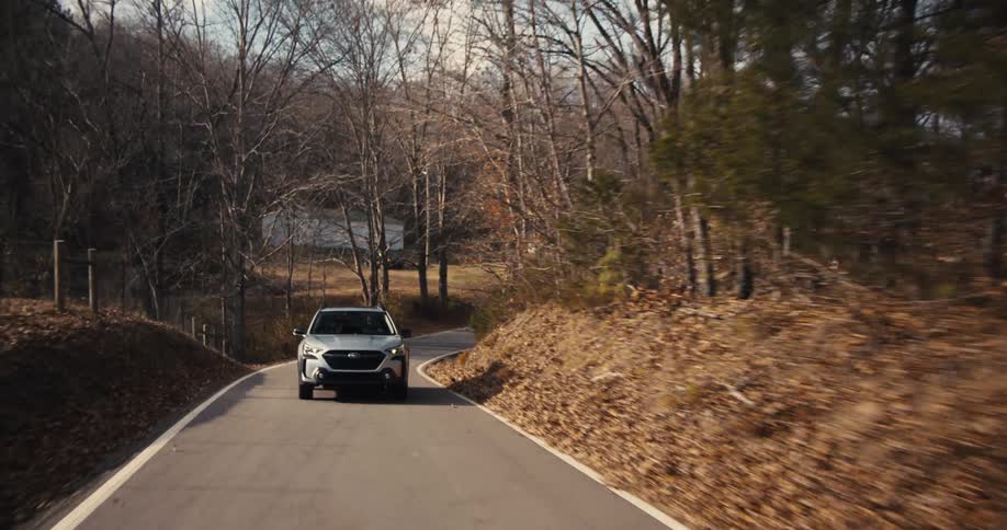 A sedan drives along a lonely road in a rural community during fall with farms and leafless trees lining the road