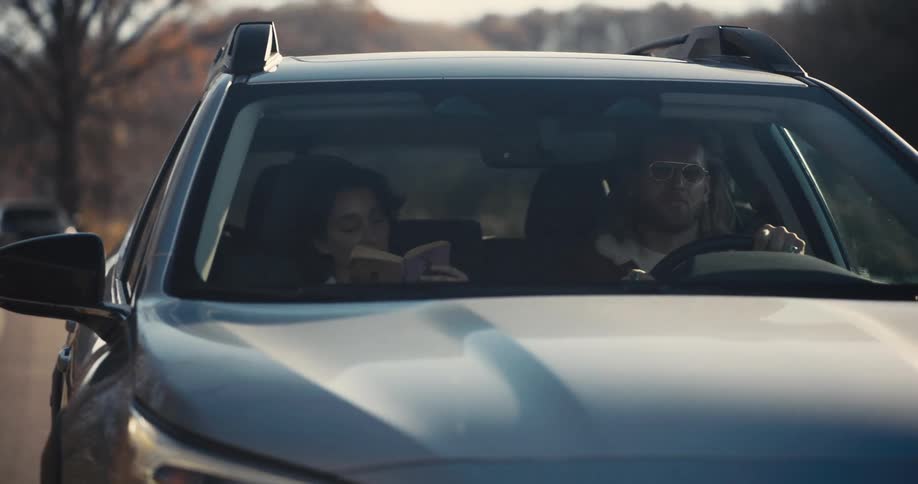 Man driving a car while the passenger beside him reads a book