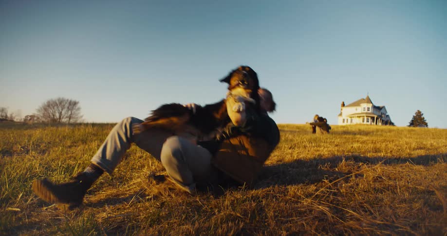 Man plays lying in the field with a dog and a mother and son in the background