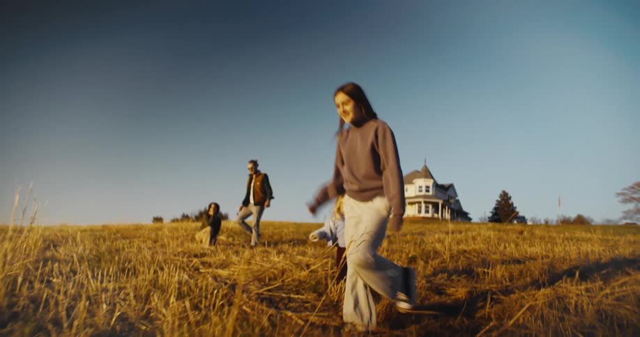 Family with children and a dog playing in a golden field near a house