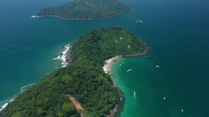 Aerial view of a lush green island with boats sailing in turquoise waters around it
