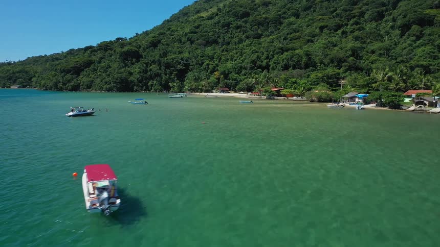 Colorful boats anchored in calm waters in front of a village surrounded by green mountains
