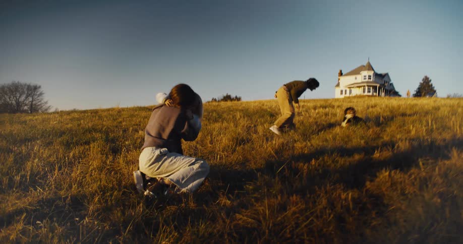 Sisters hug in the field near their rural house while their parents and dog walk away