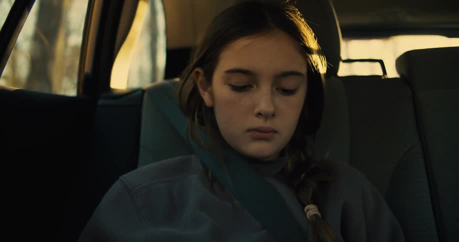 The girl is looking down as she rides in the backseat