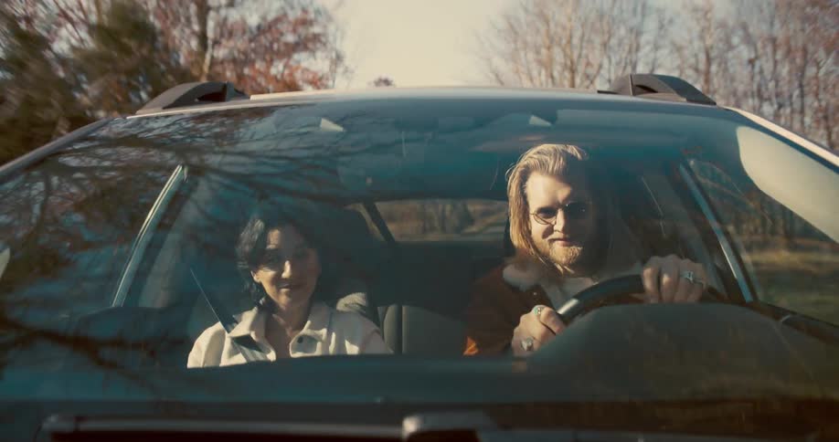 A man and woman drive together in a car on a sunny day