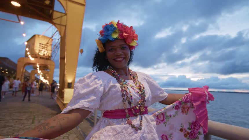 Dancer in a floral dress and flowers on her head smiling in a seaside setting