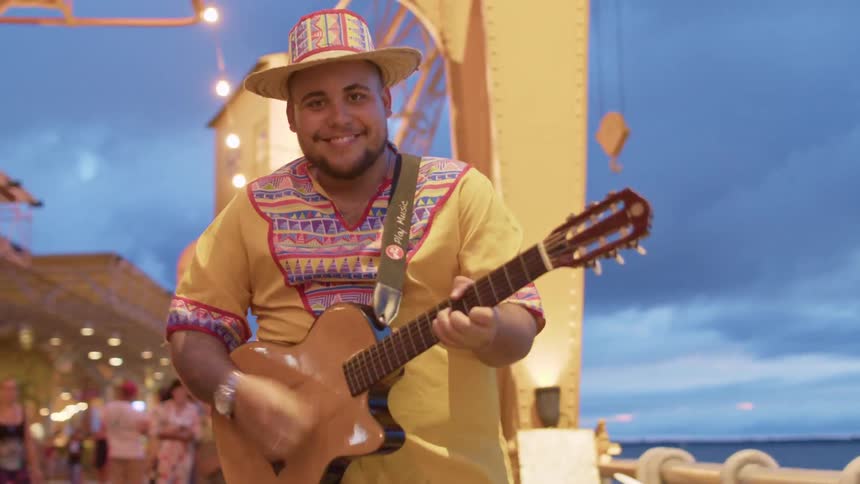 A man wearing a hat is playing a guitar on the peer while people watch