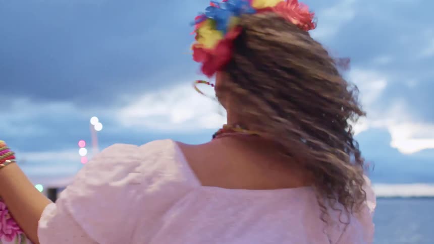 A young woman dressed in native attire excitedly spins around at a bay at midday