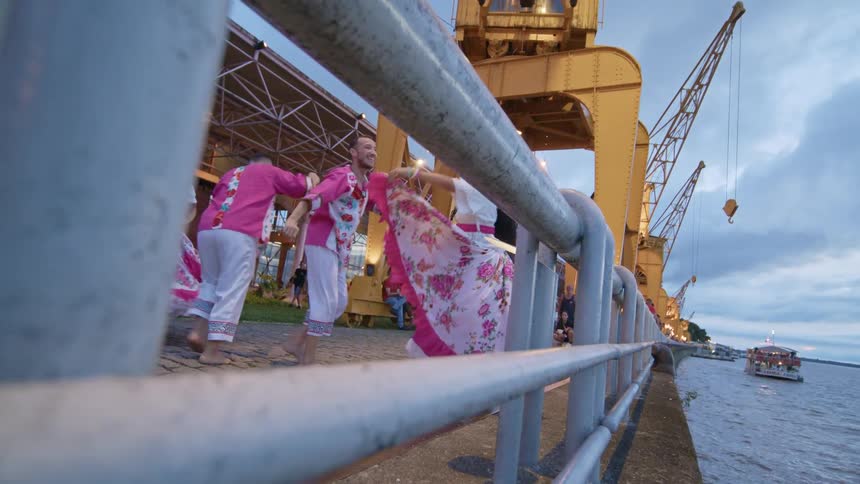 Four people dancing on a bridge over the sea wearing traditional clothes and looking happy
