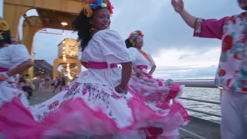 People in colorful outfits dance joyfully by the seaside