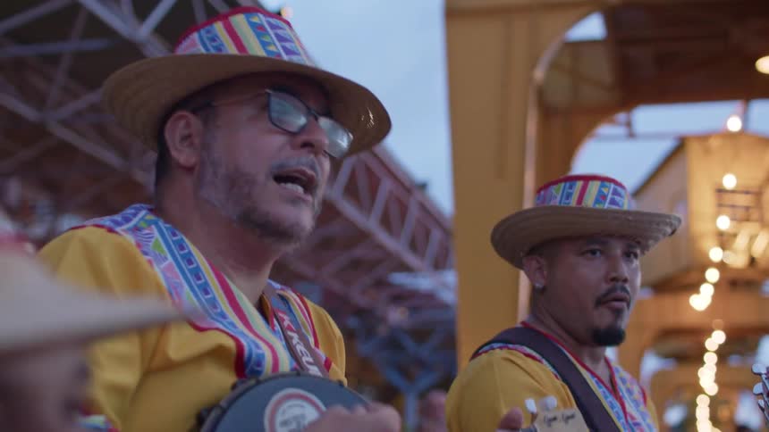 Men wearing colorful outfits and straw hats play music in an outdoor setting