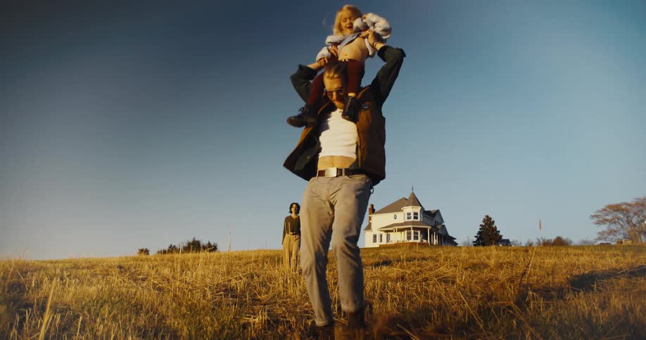 A father playfully carries his child on his shoulders in a field