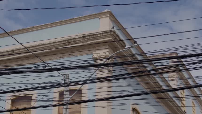 A camera is slowly panning up an old light blue building the building has many wires in front of it