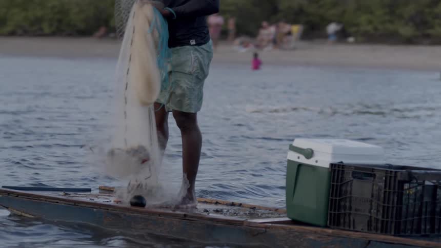 Men in a canoe fish with a net near the beach