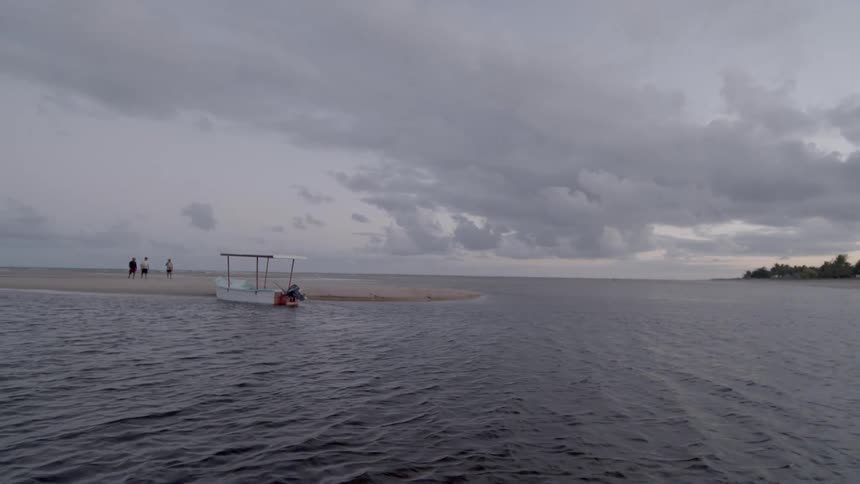 People walk on a sandbar beside a small boat in the ocean