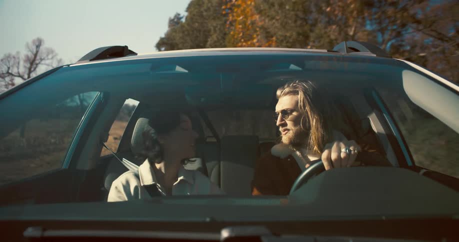 Couple travels by car on a sunny road surrounded by trees