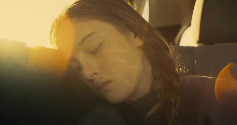 Glaring sun partially obscures a woman leaning her head against her seat
