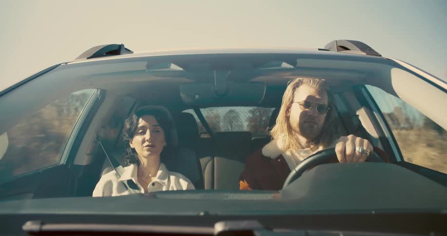 A frontfacing view of a couple in a car with the man driving and the woman as a passenger and they are holding hands