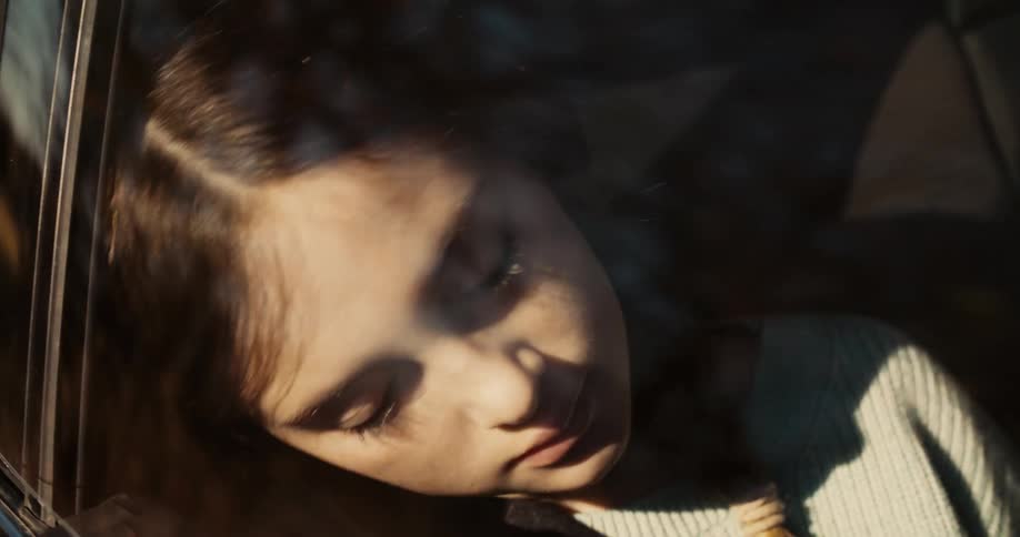 Girl rests her head on the car window while sleeping illuminated by sunlight