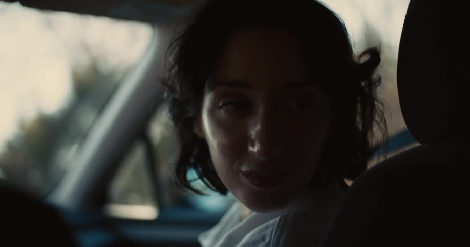Shorthaired woman looks back inside a car lit by sunlight
