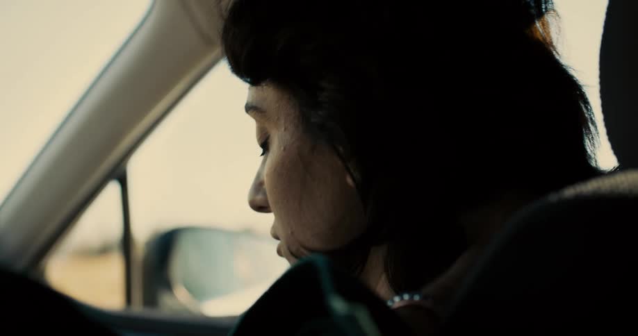 The video shows a closeup of a person sitting in the passenger seat of a car the person is looking out the window and their expression is one of contemplation or sadness