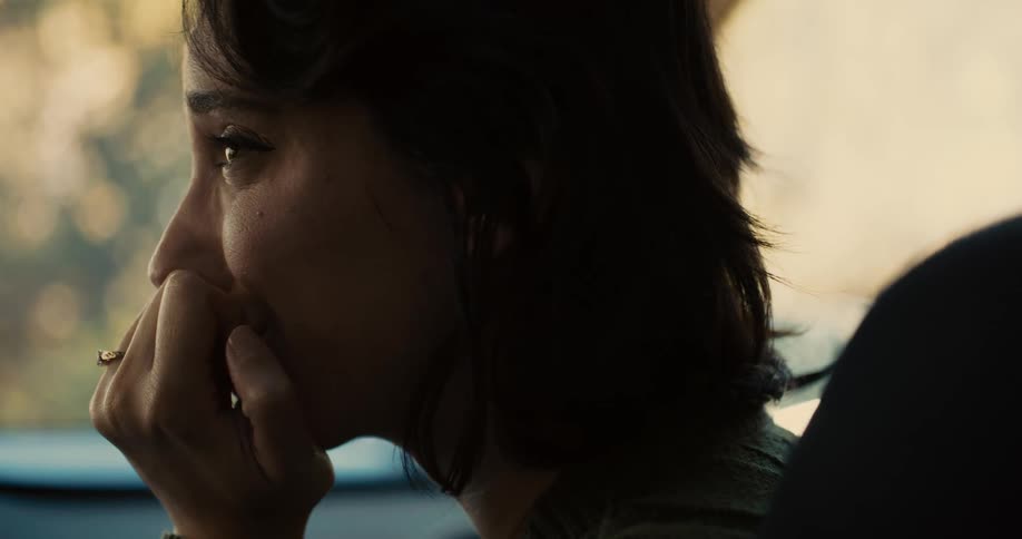 A side profile shot shows a woman with dark hair looking out of a car window she is resting her chin on her hand and appears to be in deep thought or listening intently to someone offcamera