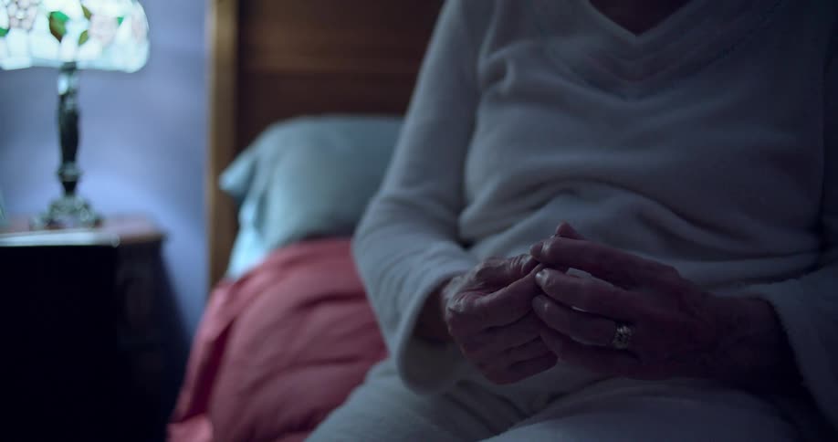 A person is seen from the waist up holding a ring and a piece of paper they are sitting on a bed next to a lit lamp