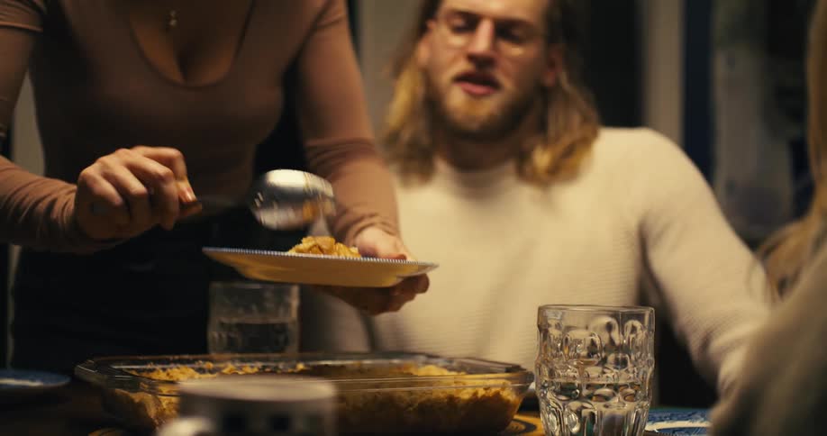 A woman serving dinner to a young man and another woman at the dining table while standing as the others remain seated