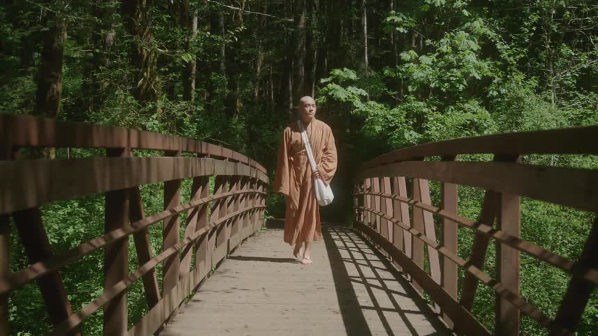 Monk walking barefoot across a wood bridge in the forest