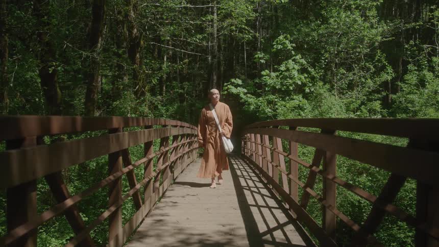 Monk walking barefoot across a bridge in a forest