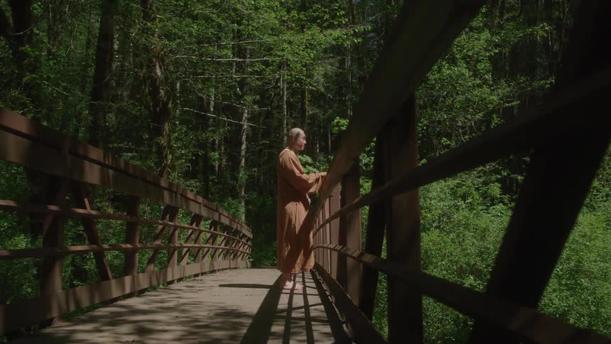 The monk is standing on the bridge looking over the side